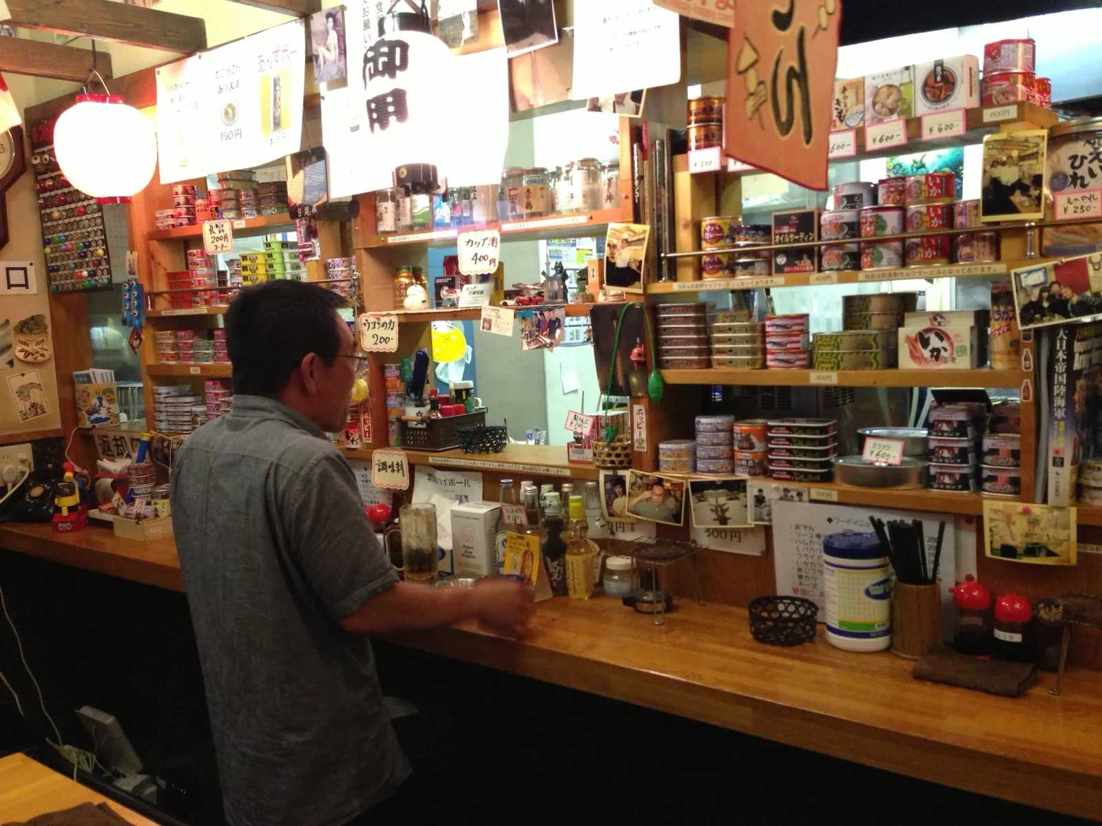 A small bar in Tokyo: a man at the counter, shelves full of canned food behind it